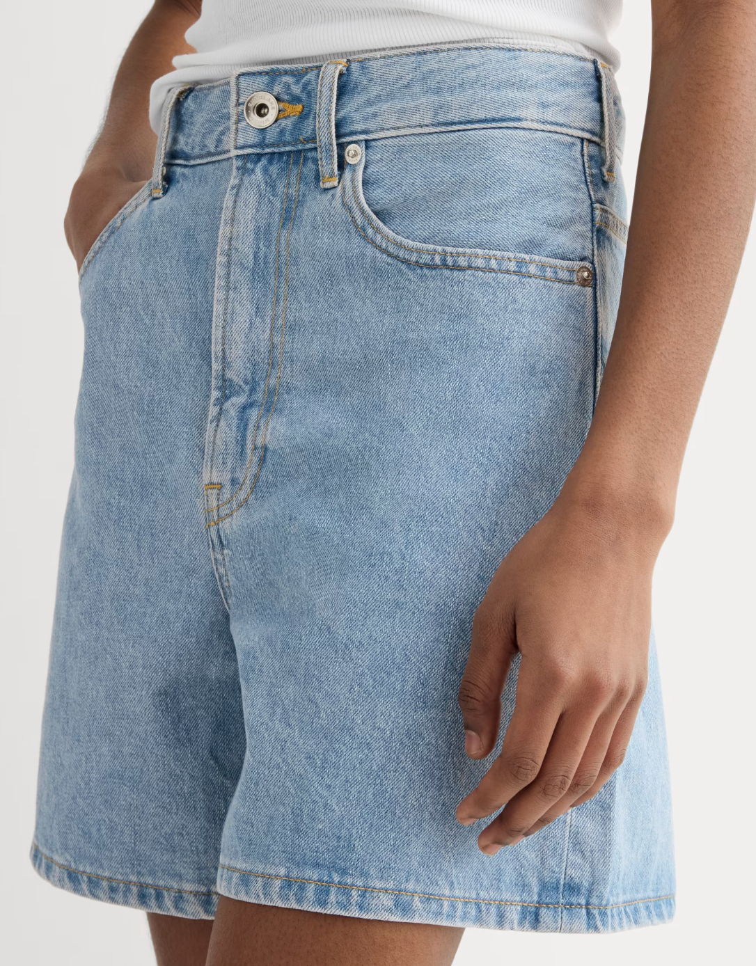 Person wearing high-waisted denim shorts with hands in pockets, styled with a white top