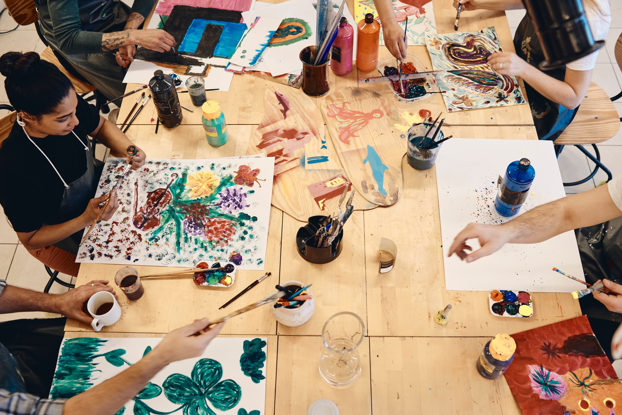 People sit around a table painting on large sheets of paper with brushes, creating various colorful abstract designs