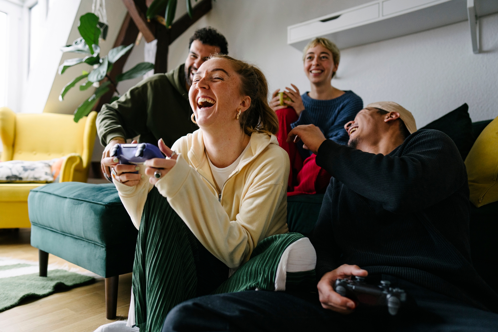 Four people laughing and playing video games on a couch in a living room