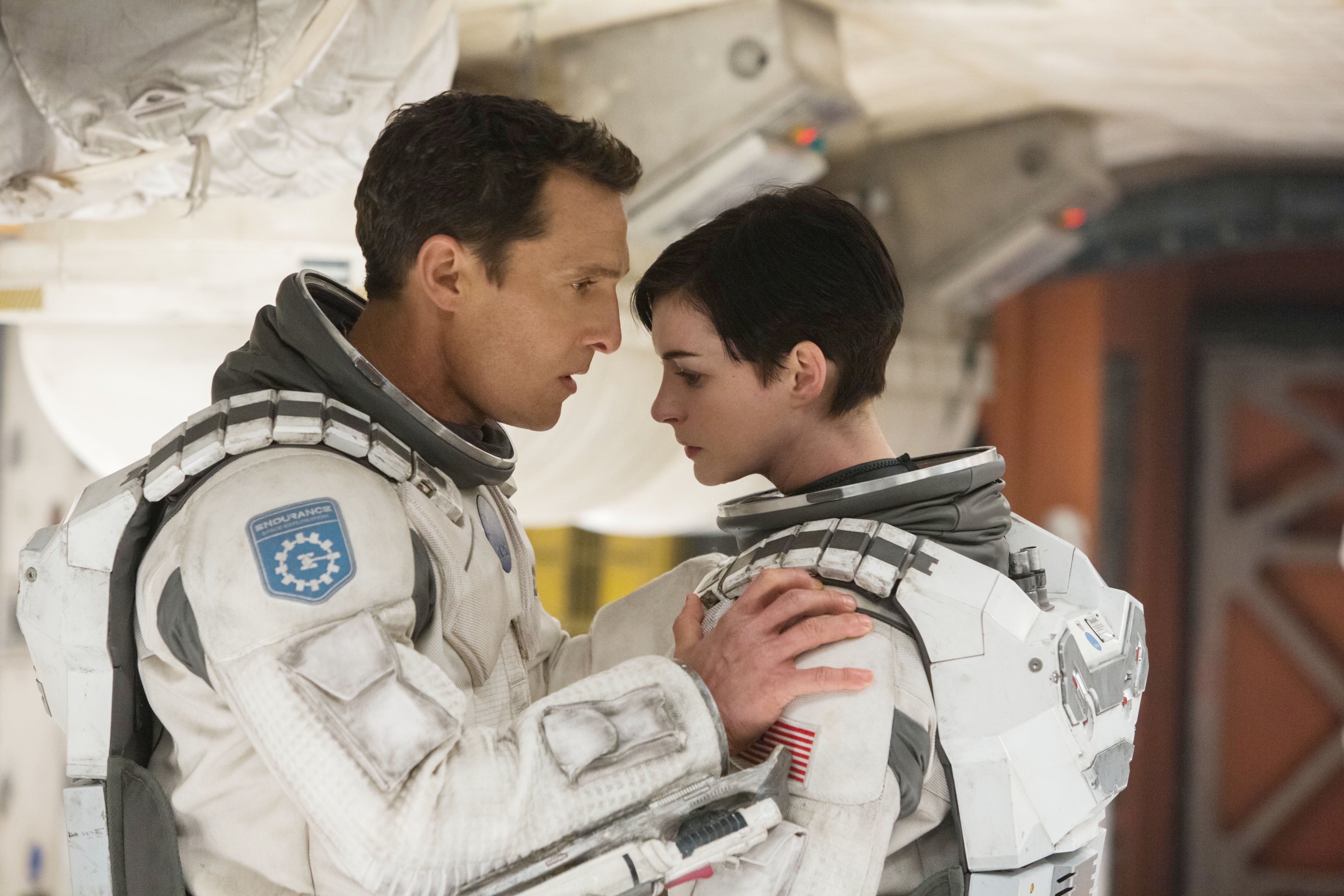 Two astronauts in suits face each other intensely in a space station setting, suggesting a moment of connection