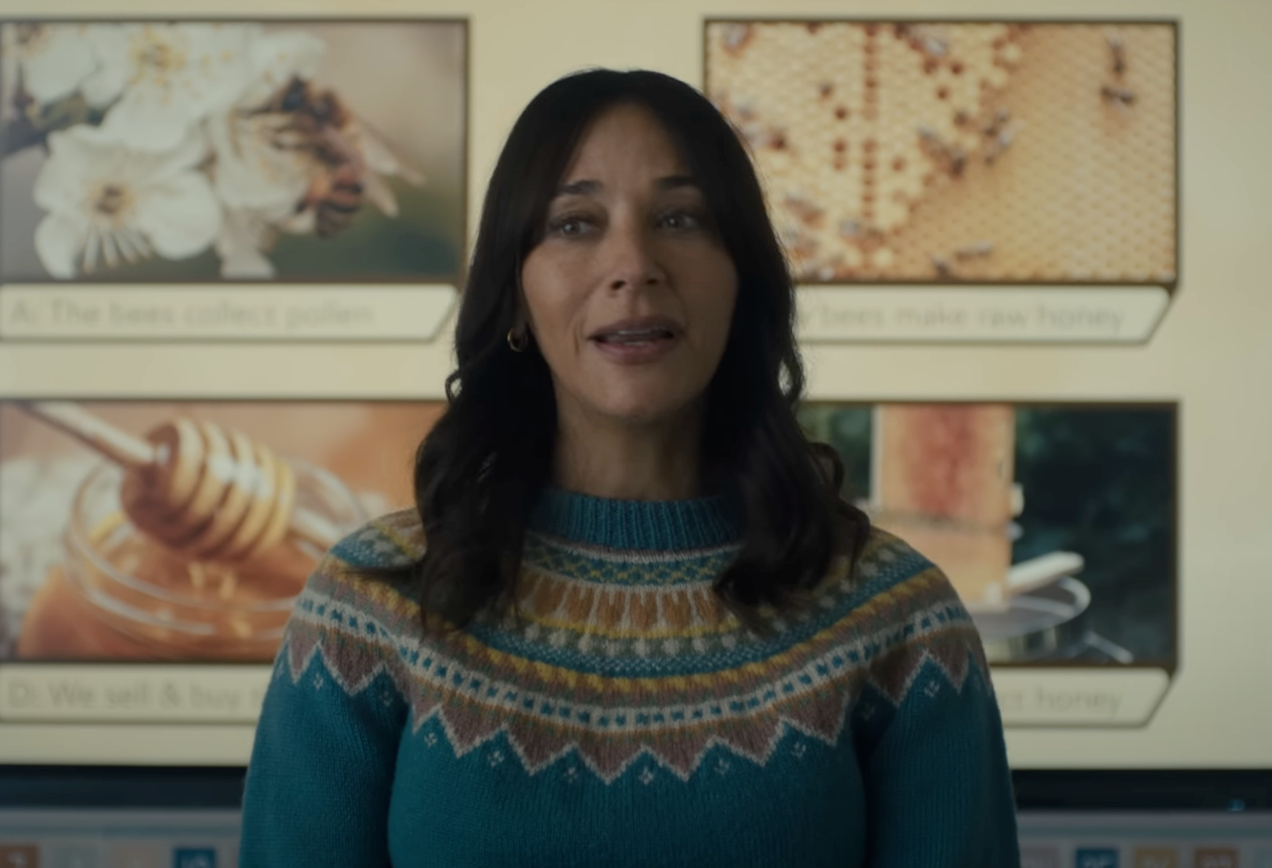 Person in a patterned sweater stands in front of a presentation showing bees and honey-related images