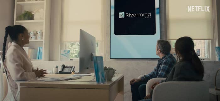 Three people in an office look at a large screen displaying "Rivermind Lux" with the Netflix logo in the corner