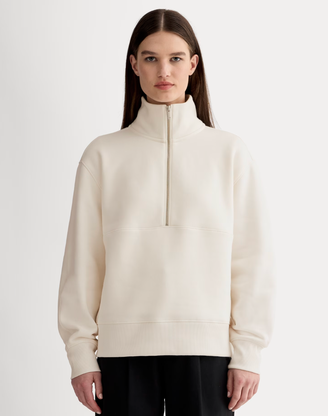 model wearing a minimalist high-neck pullover, front zipper, styled with black pants