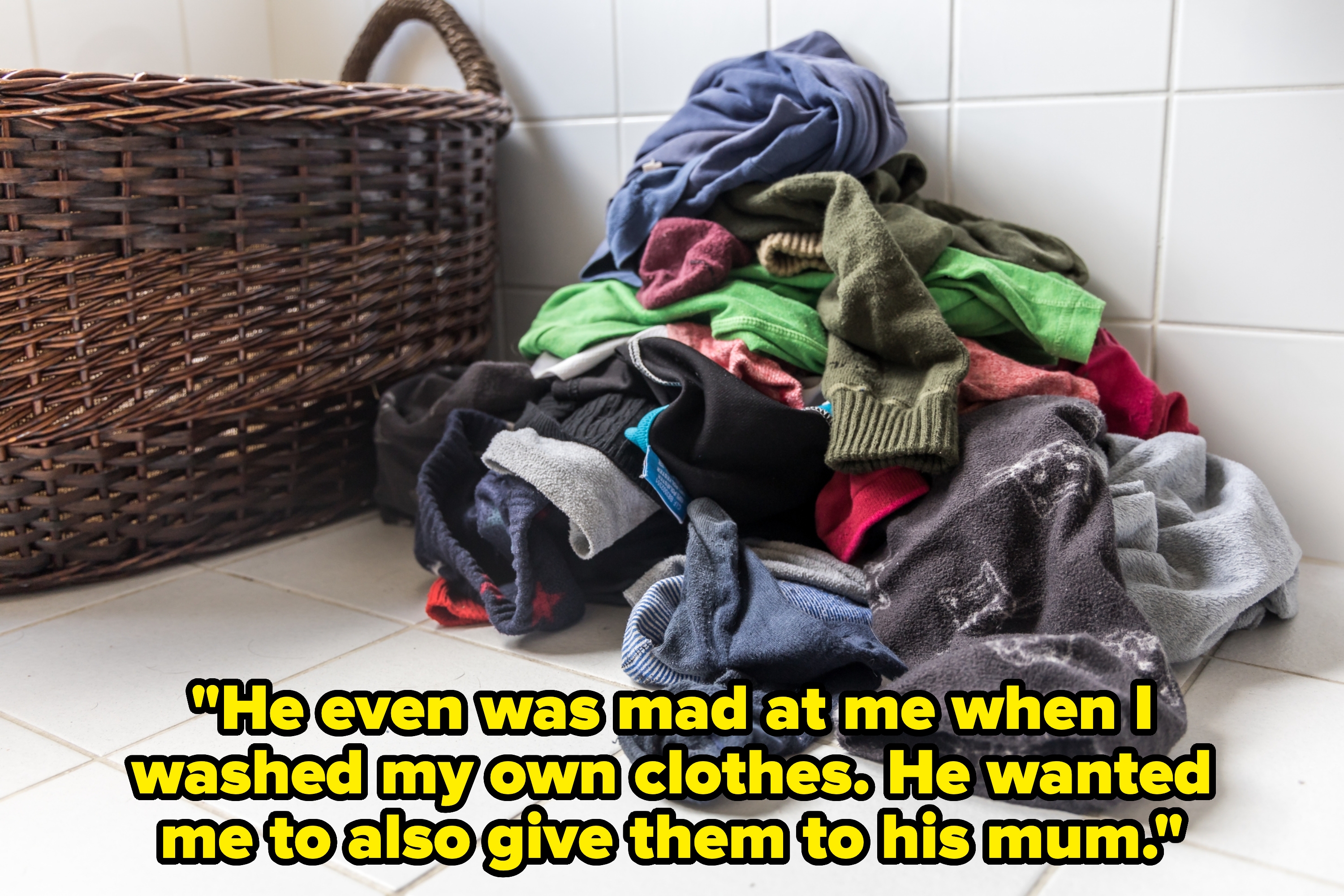 Pile of assorted clothes on the floor next to a wicker laundry basket, in a bathroom setting