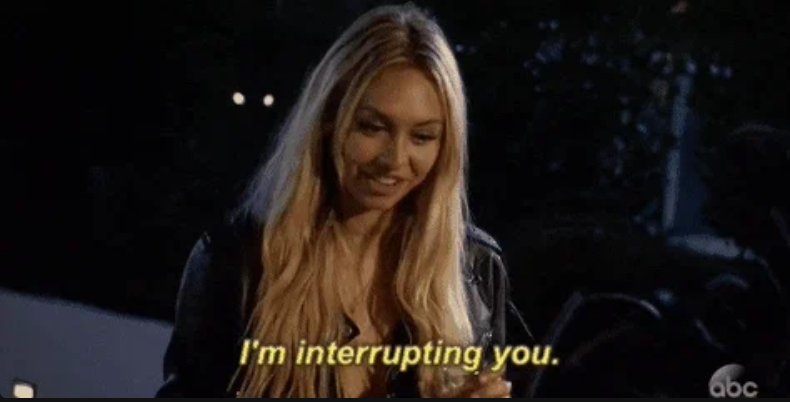 A person with long hair smiling while holding a drink. Subtitles read: "I'm interrupting you."