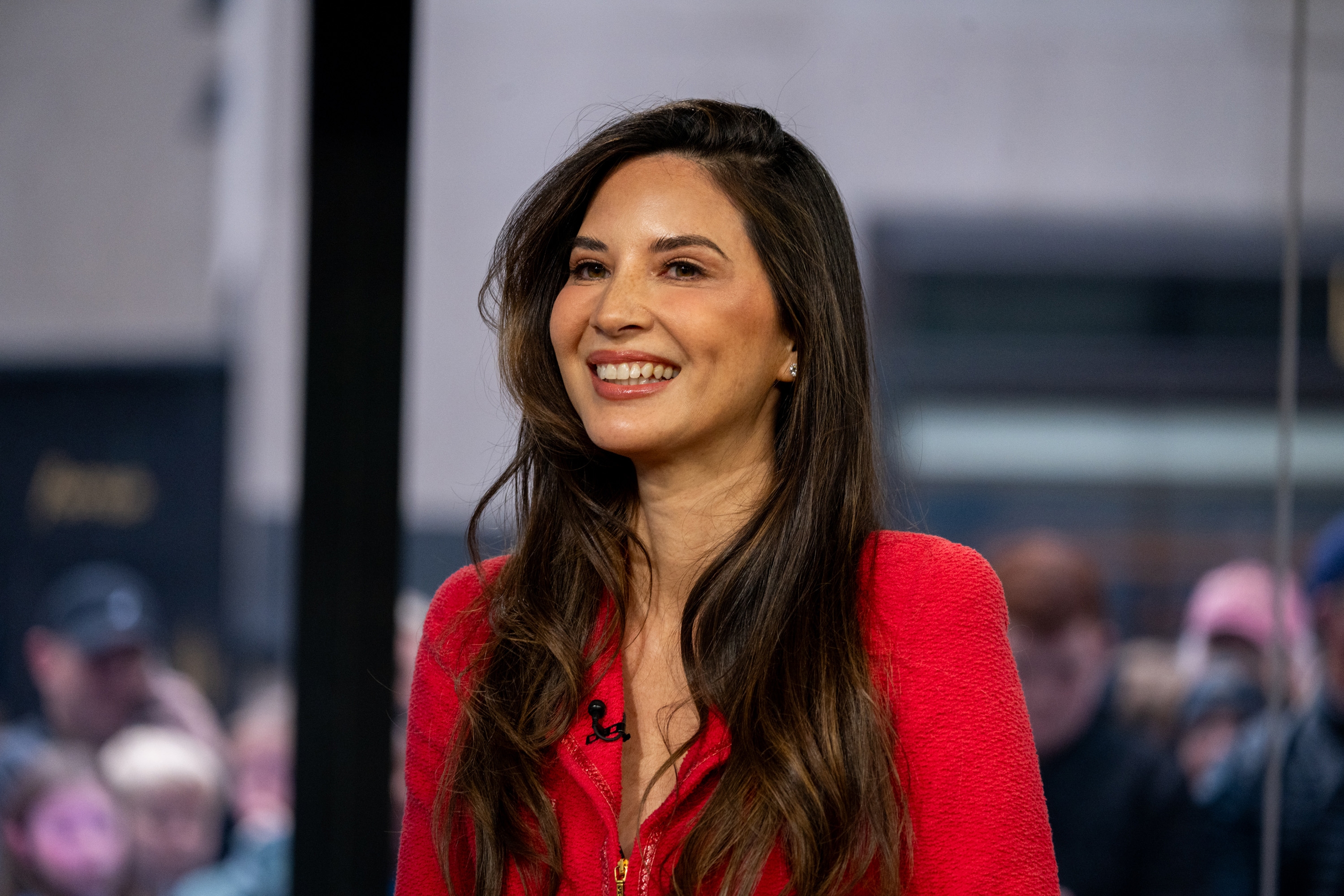 Woman smiling in a studio interview setting, wearing a stylish fitted outfit