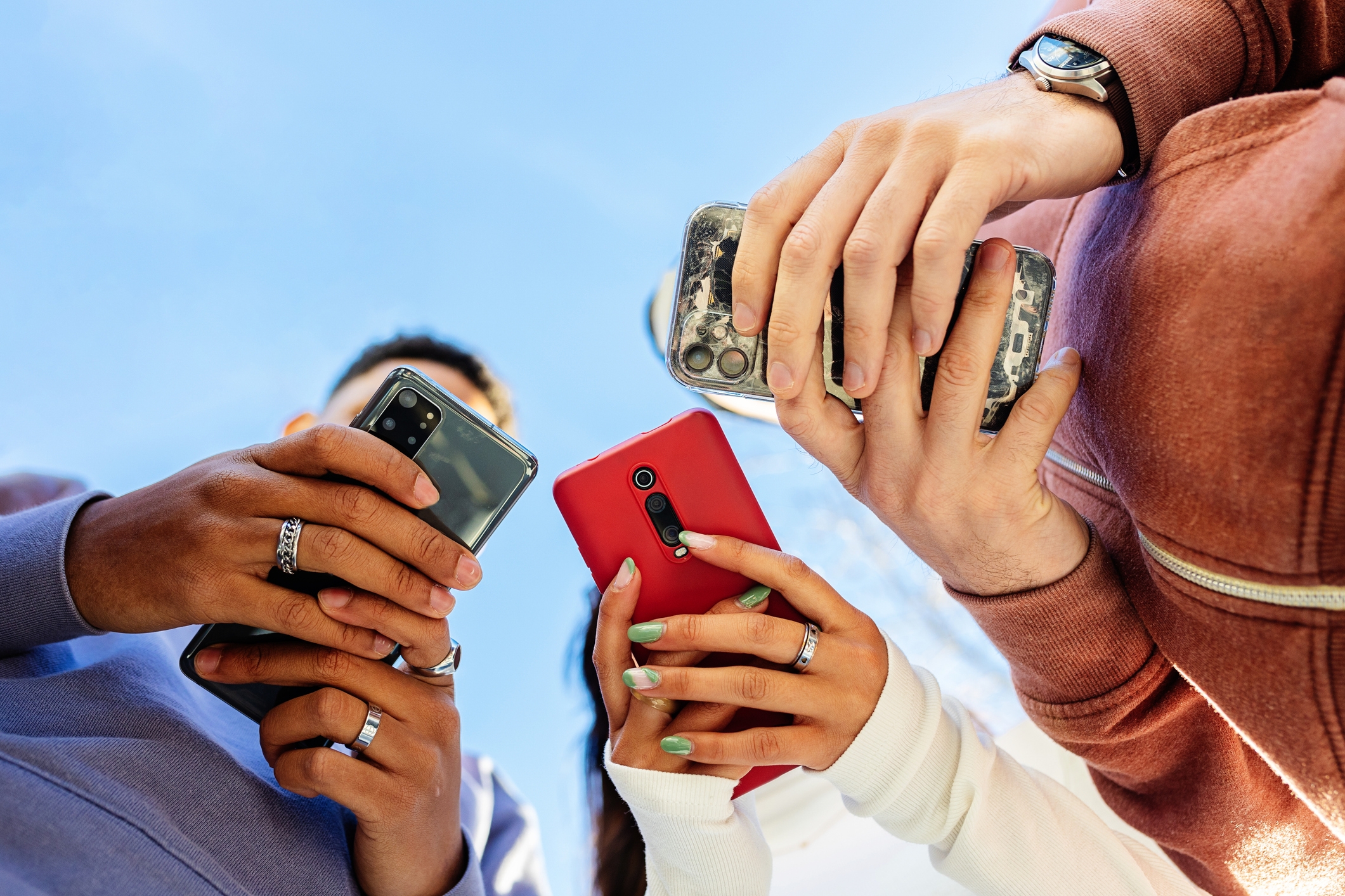People holding smartphones, viewed from below, with hands showing various rings