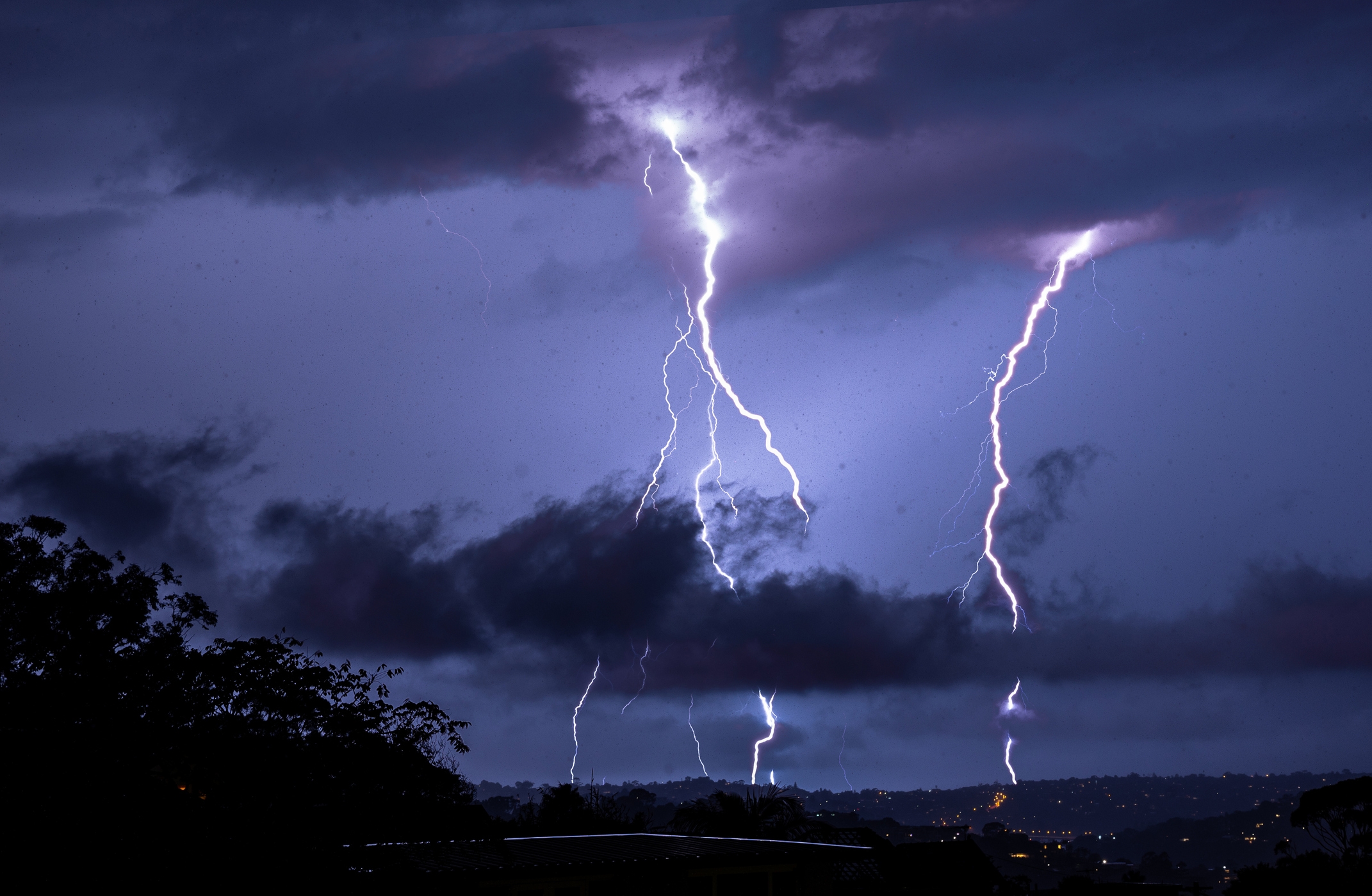 Several bright lightning bolts illuminate a dark, stormy sky over a landscape at night