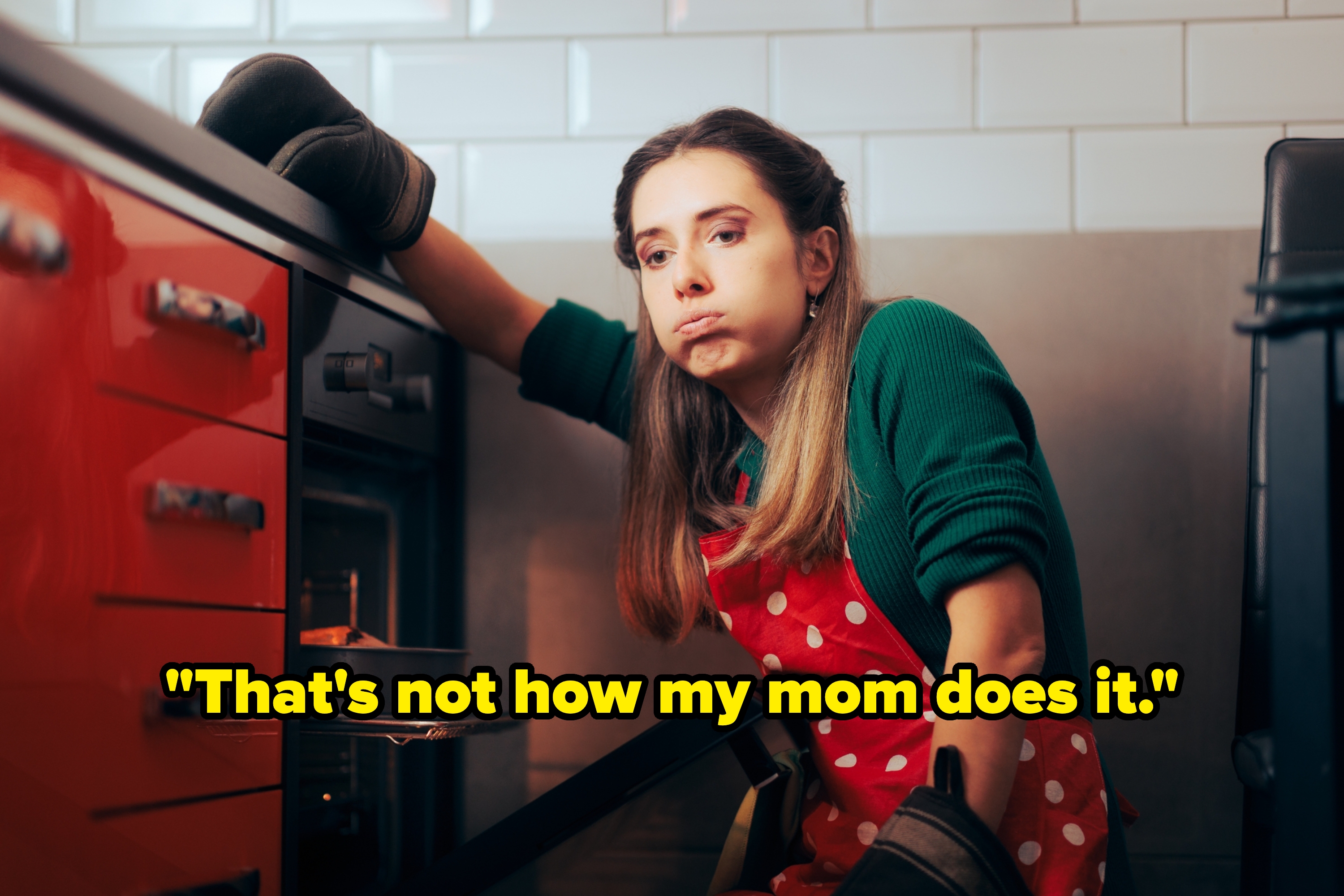 Person in kitchen with oven open, wearing an apron and oven mitts, looking tired or frustrated