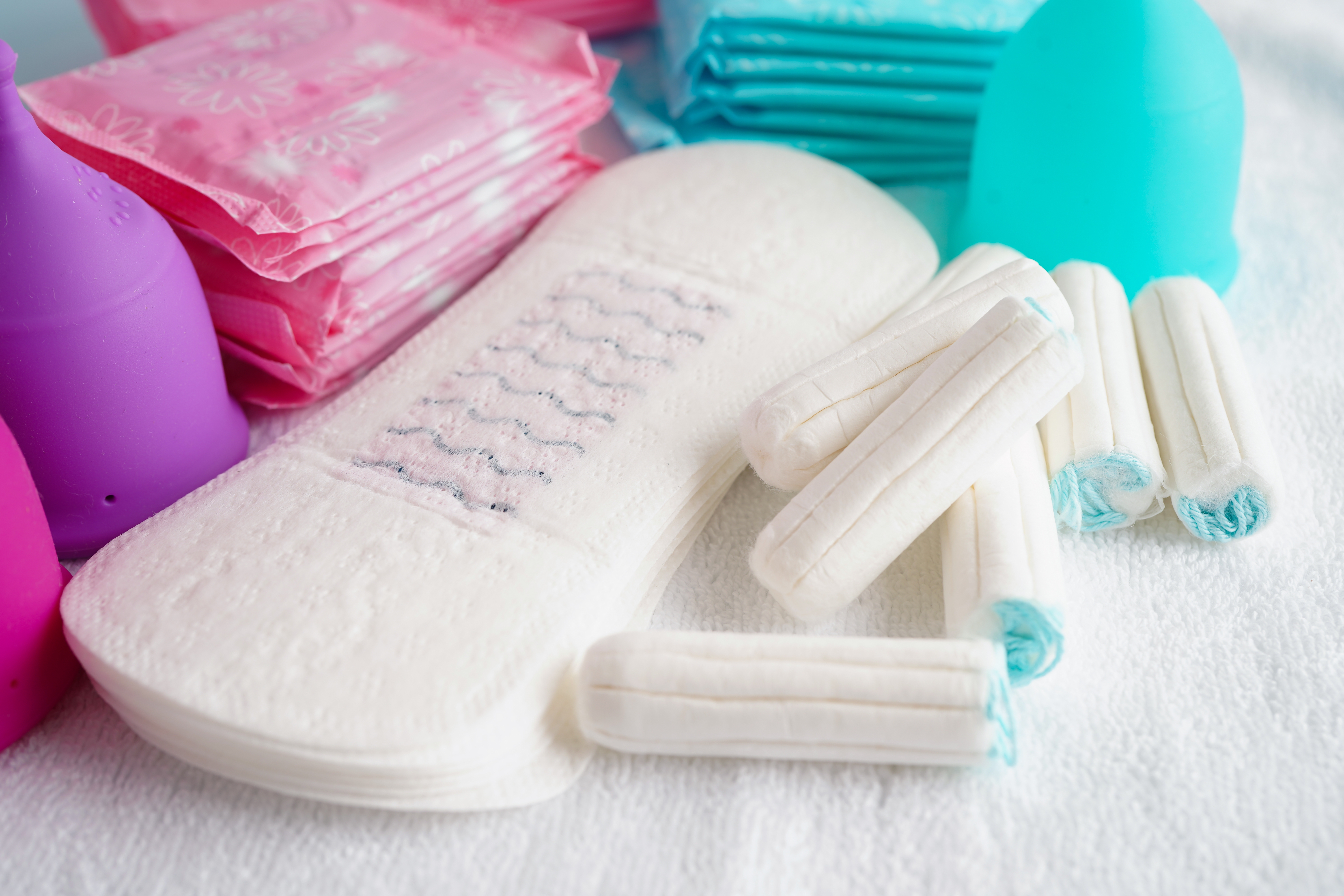 Ulike menstruasjonsprodukter, inkludert pads, tamponger og menstruasjonskopper, vises på en hvit overflate