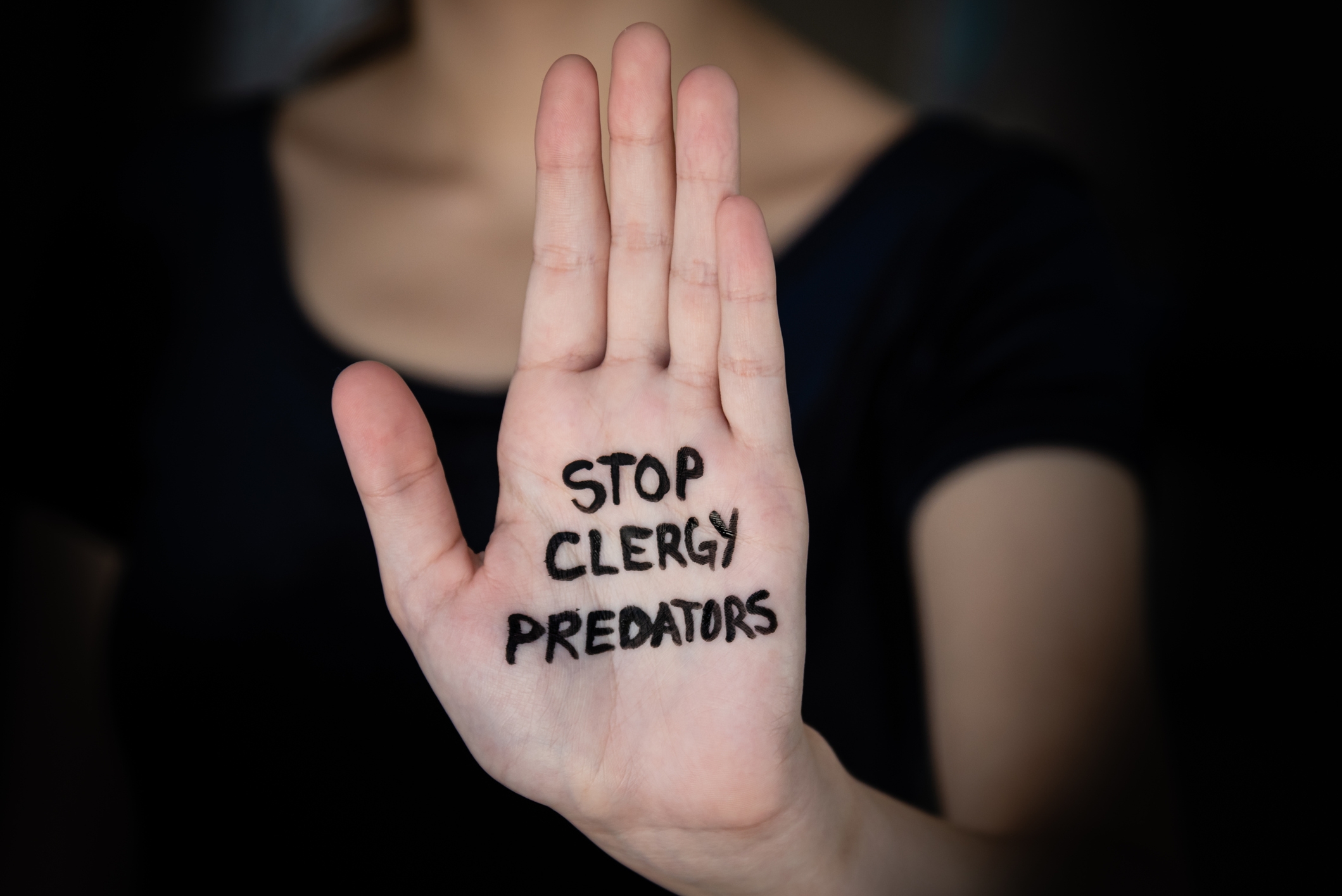 Hand with "Stop Clergy Predators" written on the palm, raised in a gesture of protest