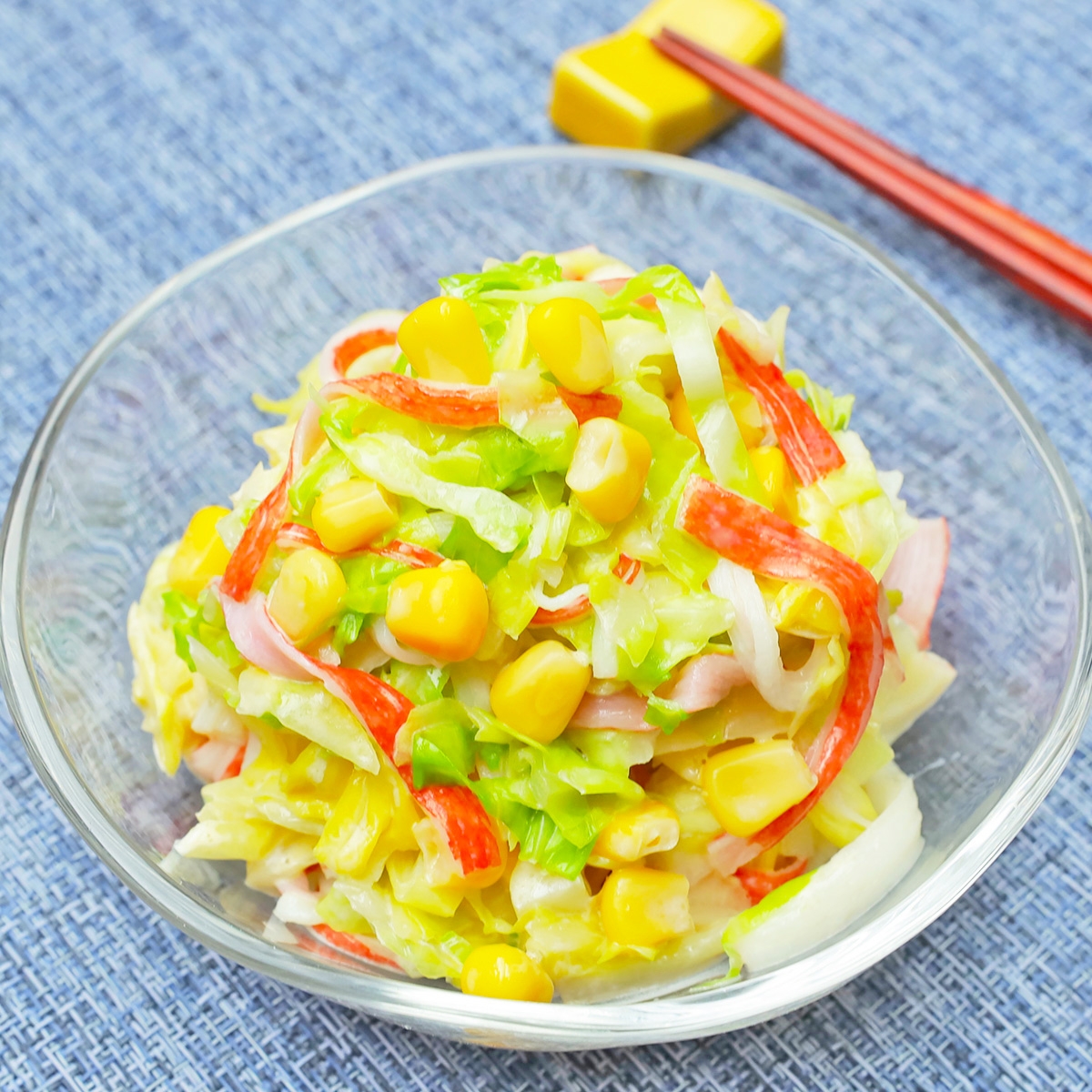 ガラスのボウルに盛られたサラダ。コーン、カニカマ、レタスが混ざり、新鮮な印象の料理。