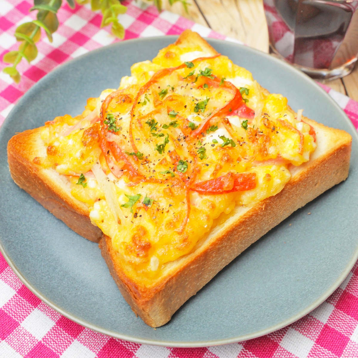 チーズトーストにトマトとパセリがトッピングされ、プレートにのせられています。ピクニック風の背景。