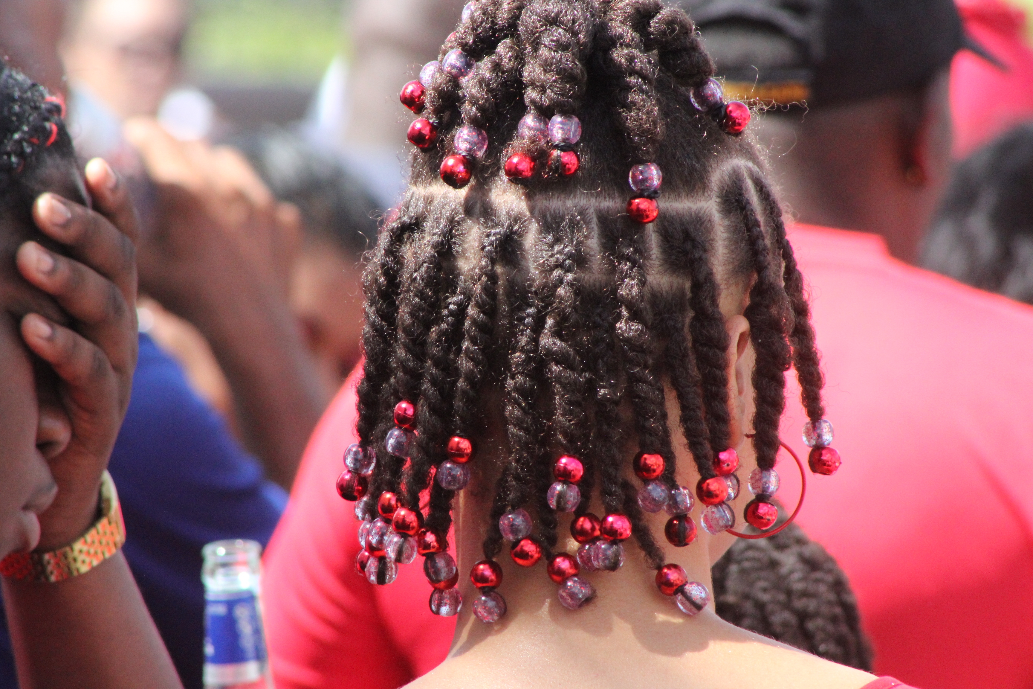 Person with intricately braided hair adorned with red beads in a crowd