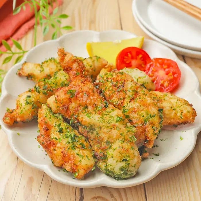 揚げた魚のフライが皿に盛られ、レモンとトマトが添えられている。