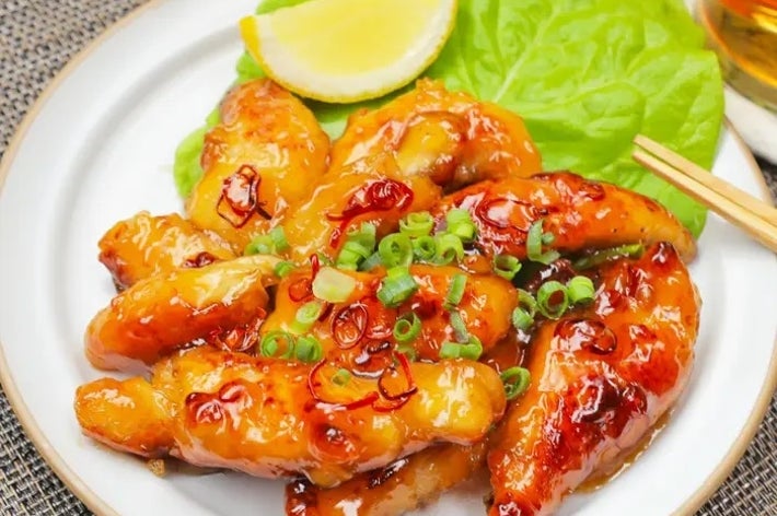 皿に盛られた照り焼きチキン。レタスとレモンが添えられ、刻んだネギがトッピングされています。