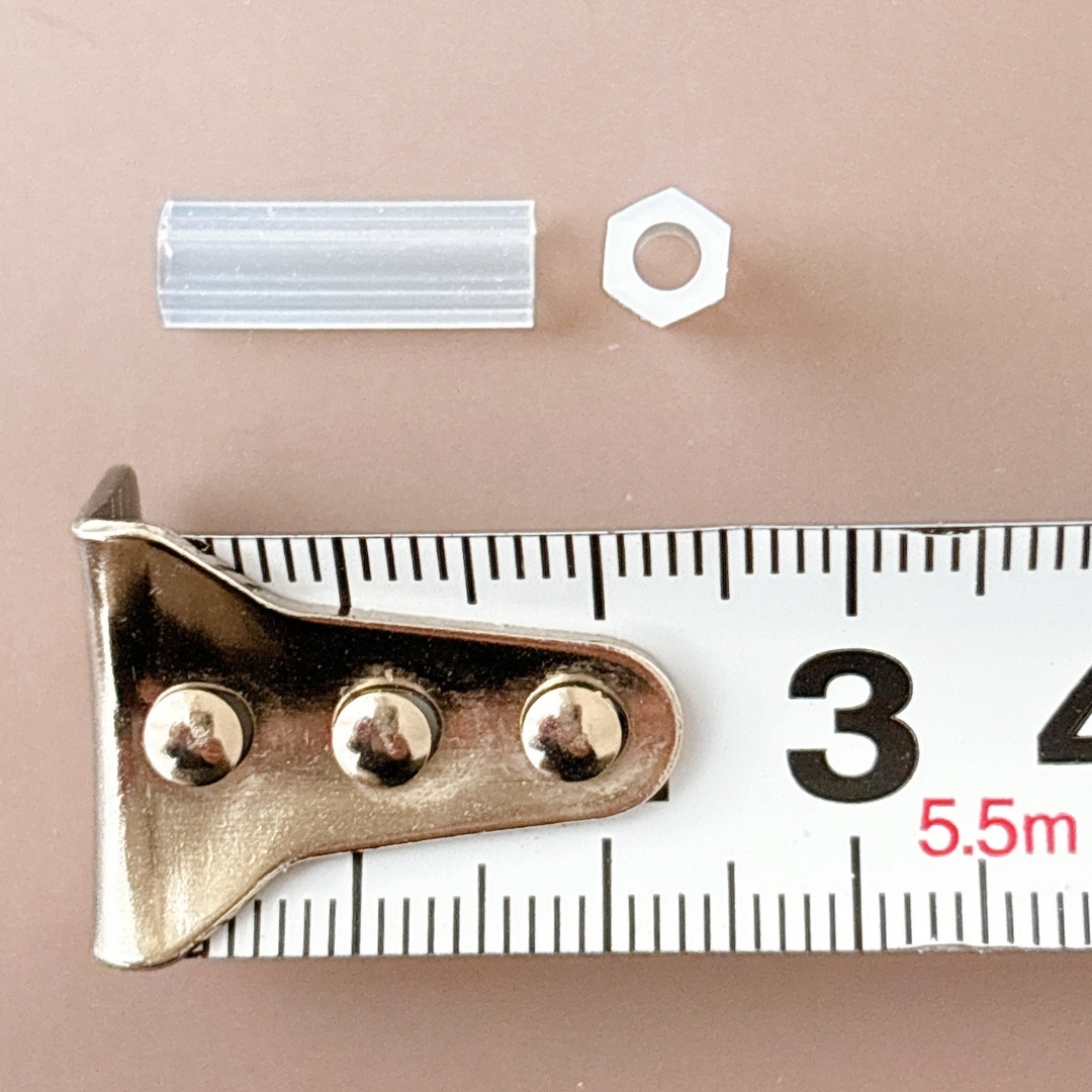 ナット、プラスチックパーツ、巻尺が並べられた画像。測定中の場面を示しています。