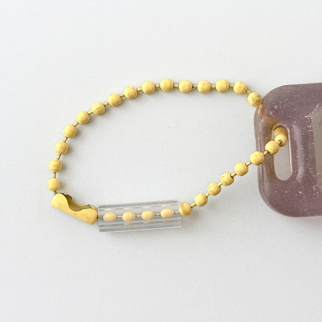 金色のビーズのキーホルダーが透明なタグに付いている。シンプルでエレガントなデザイン。