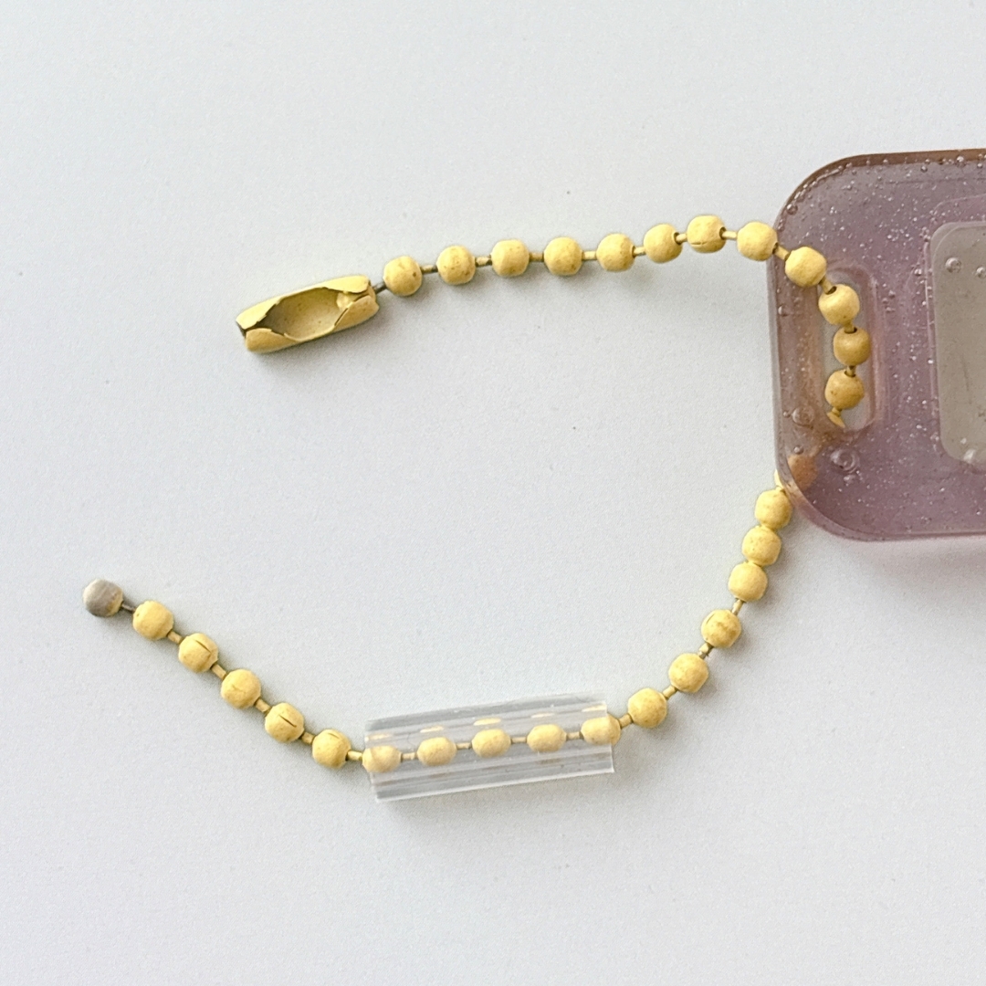 ブレスレット風のアイテムが平面に置かれている。ビーズが連続して並び、金属パーツが付いている。