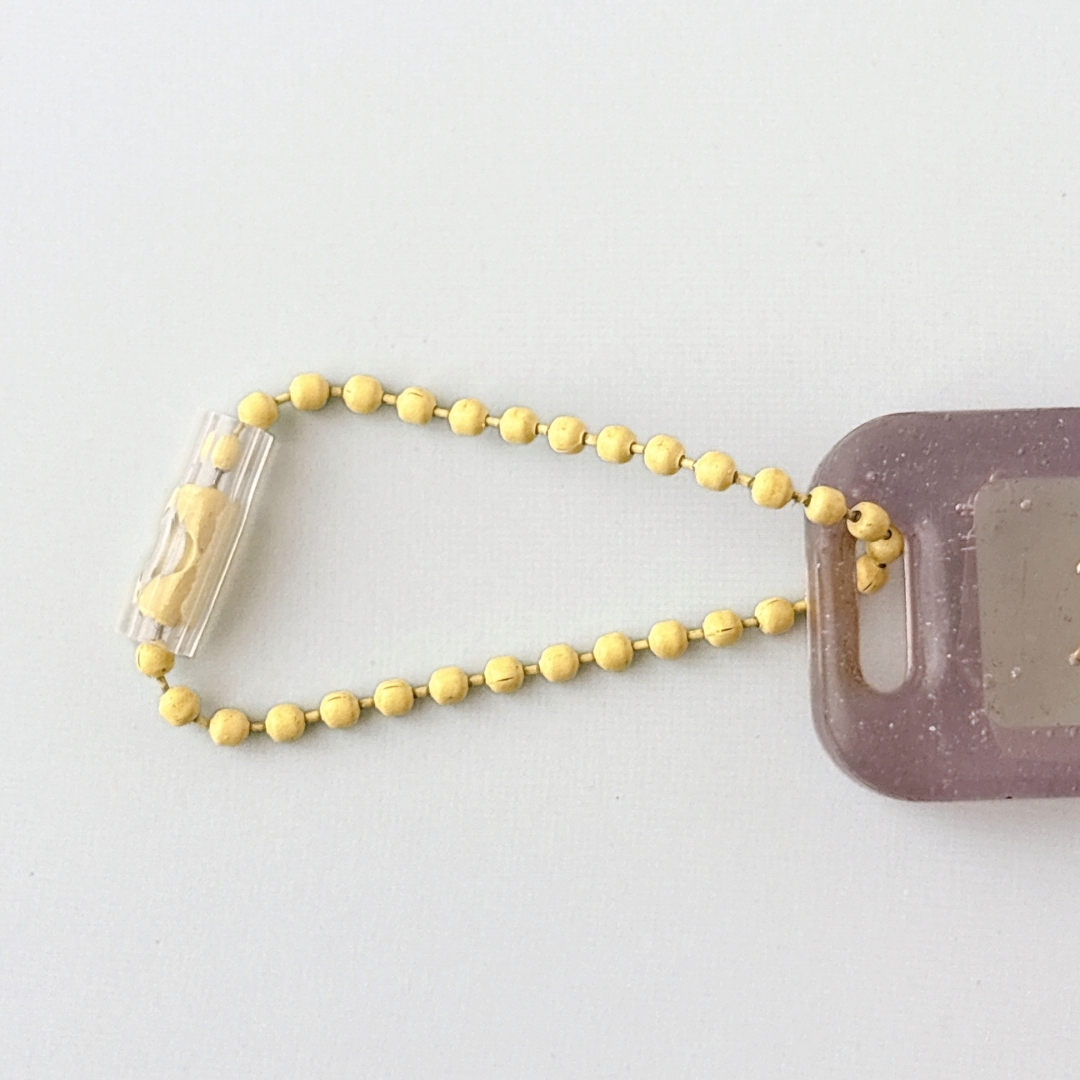 透明な管に円形の黄色いビーズが連なったチェーンとプラスチックのタグ。