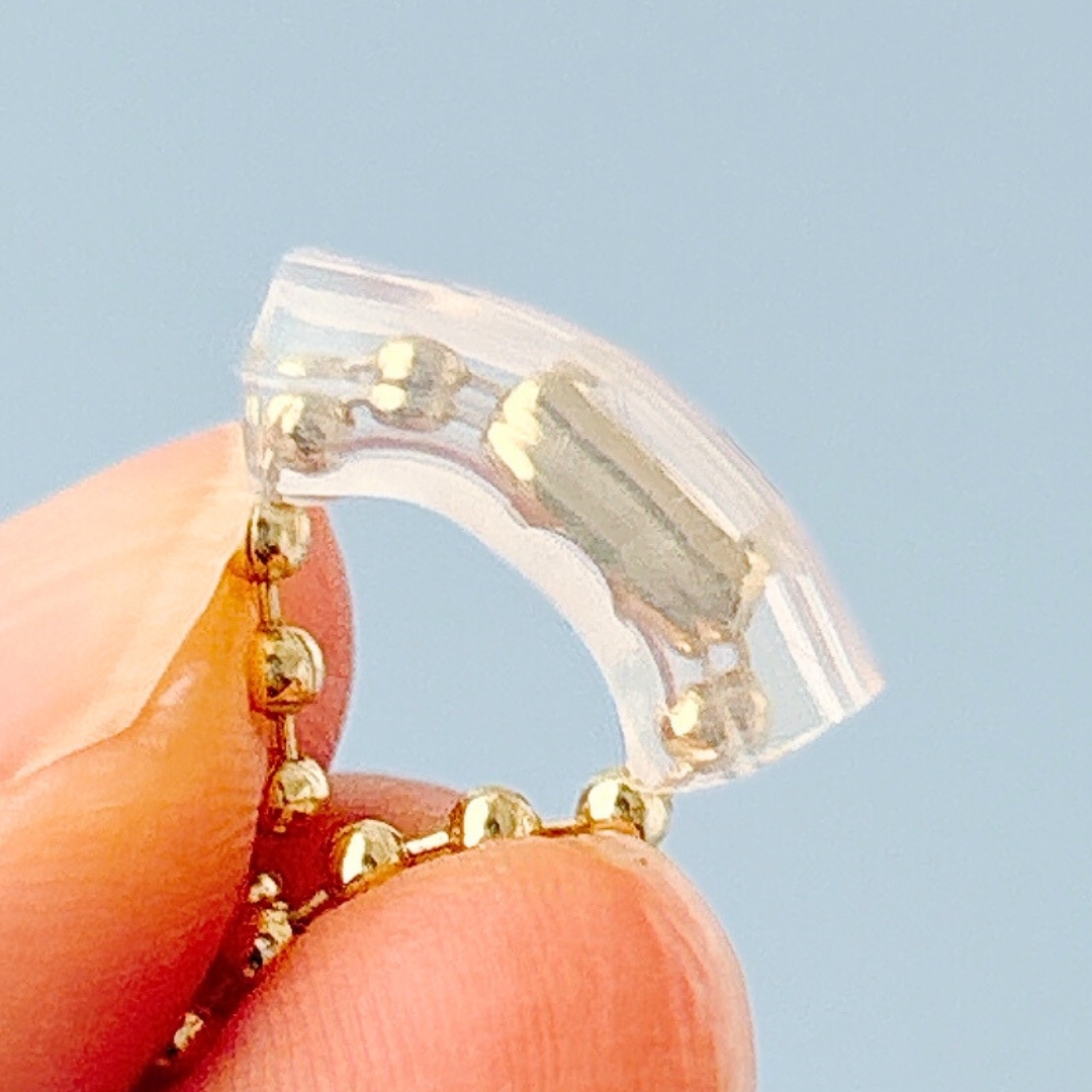 手に持たれた透明の小型補聴器で、軽量で目立たないデザインが特徴です。
