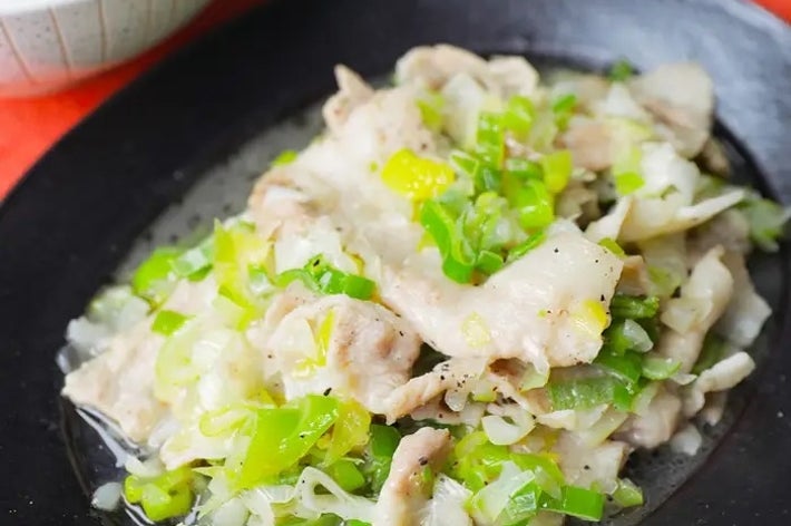 豚肉とネギを盛り付けた黒い皿。背景にご飯が少し見える。