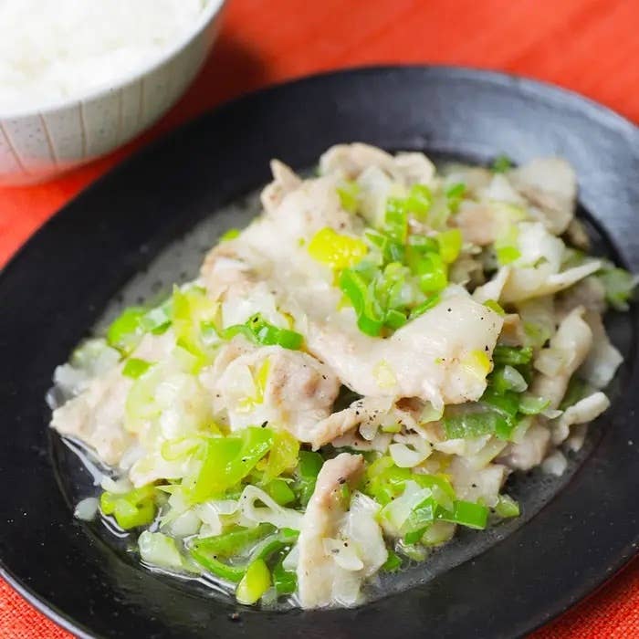皿に盛られた豚肉とたっぷりのネギ炒め、背景にはご飯の入った器。