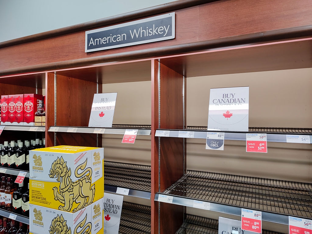 Empty store shelves under an "American Whiskey" sign, with signs encouraging buying Canadian whisky