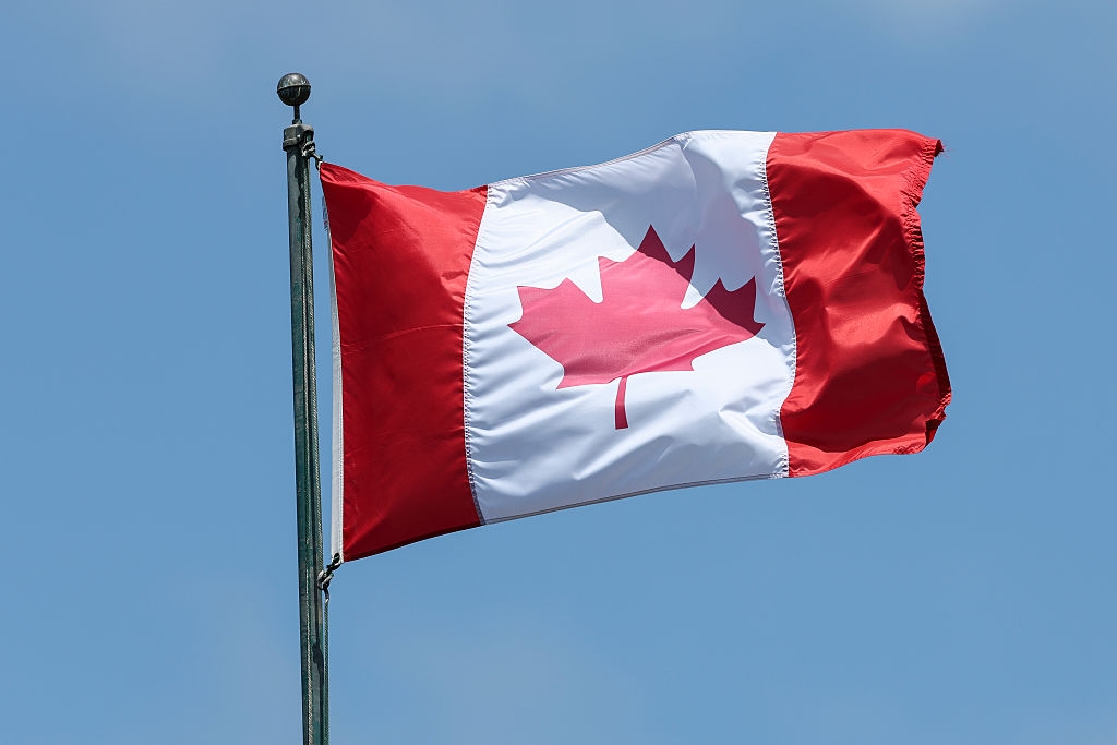 The Canadian flag flies on a pole against a clear sky, symbolizing national identity and pride