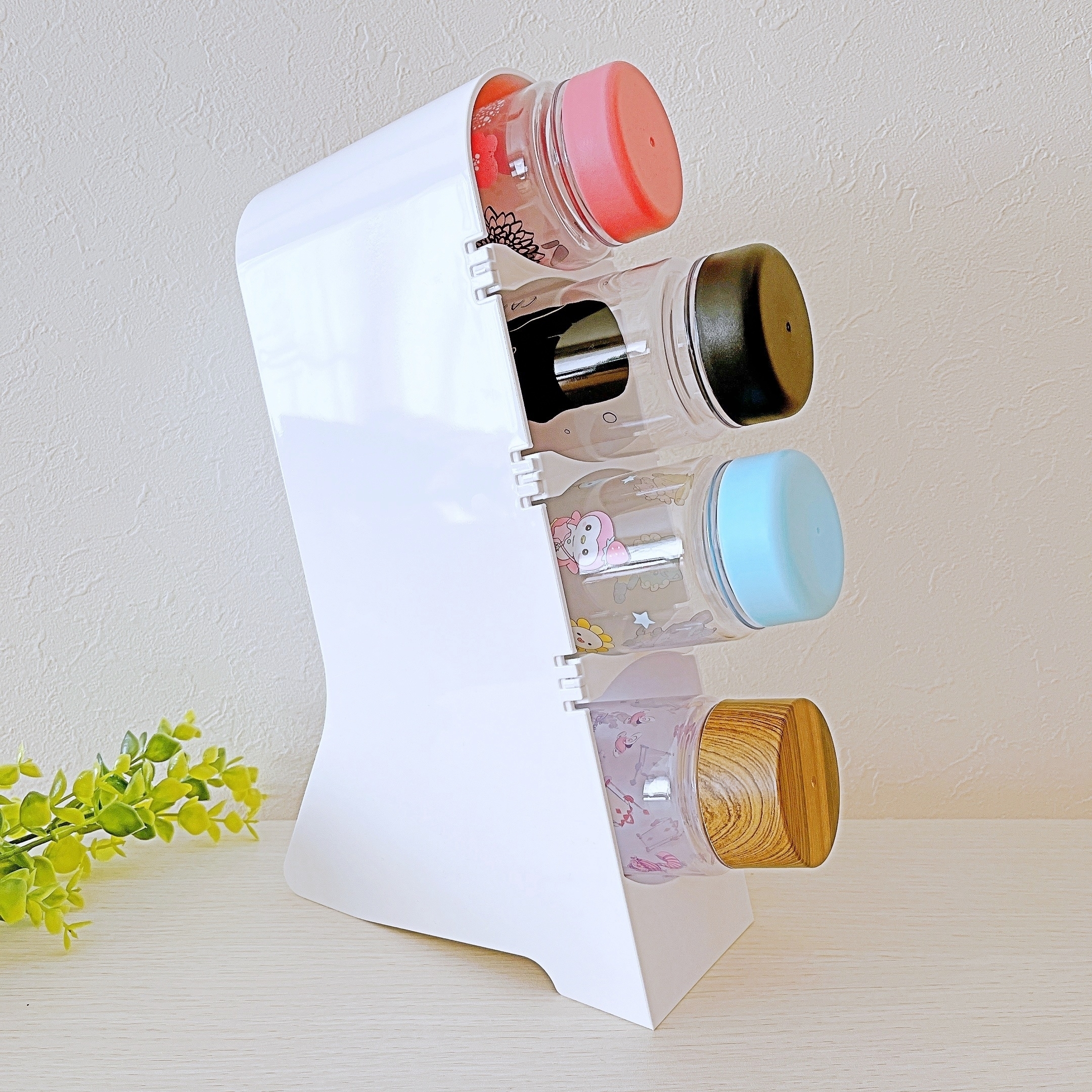 複数の小物が入った透明な容器が斜めに並んだ白いラック。シンプルなインテリアとして配置。