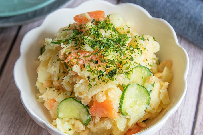 ポテトサラダが白いボウルに盛られている。きゅうりと人参が入り、上にパセリが散らされている。テーブルにはお箸が置かれている。