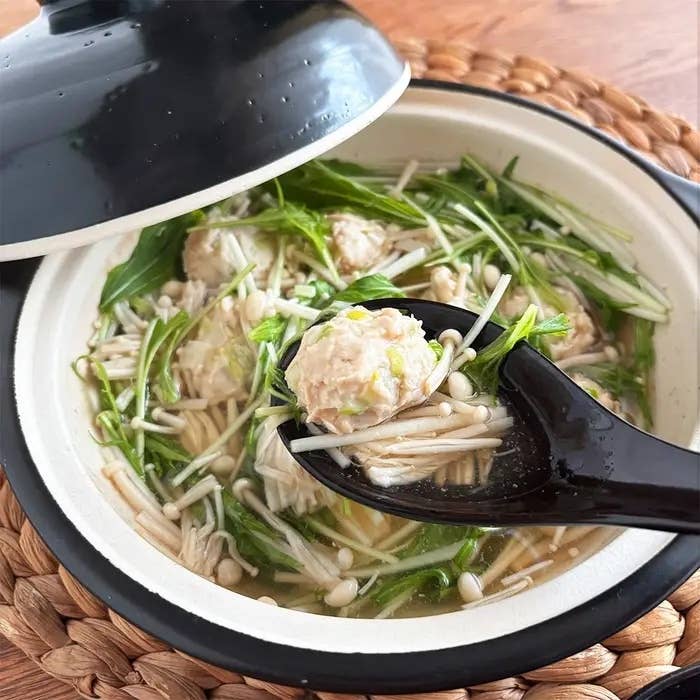 土鍋に入った鍋料理。えのきや野菜とともに、黒いスプーンで肉団子がすくわれている様子。