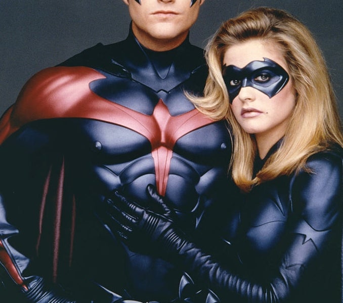 Two individuals dressed as superheroes wearing masks and form-fitting suits, posing confidently