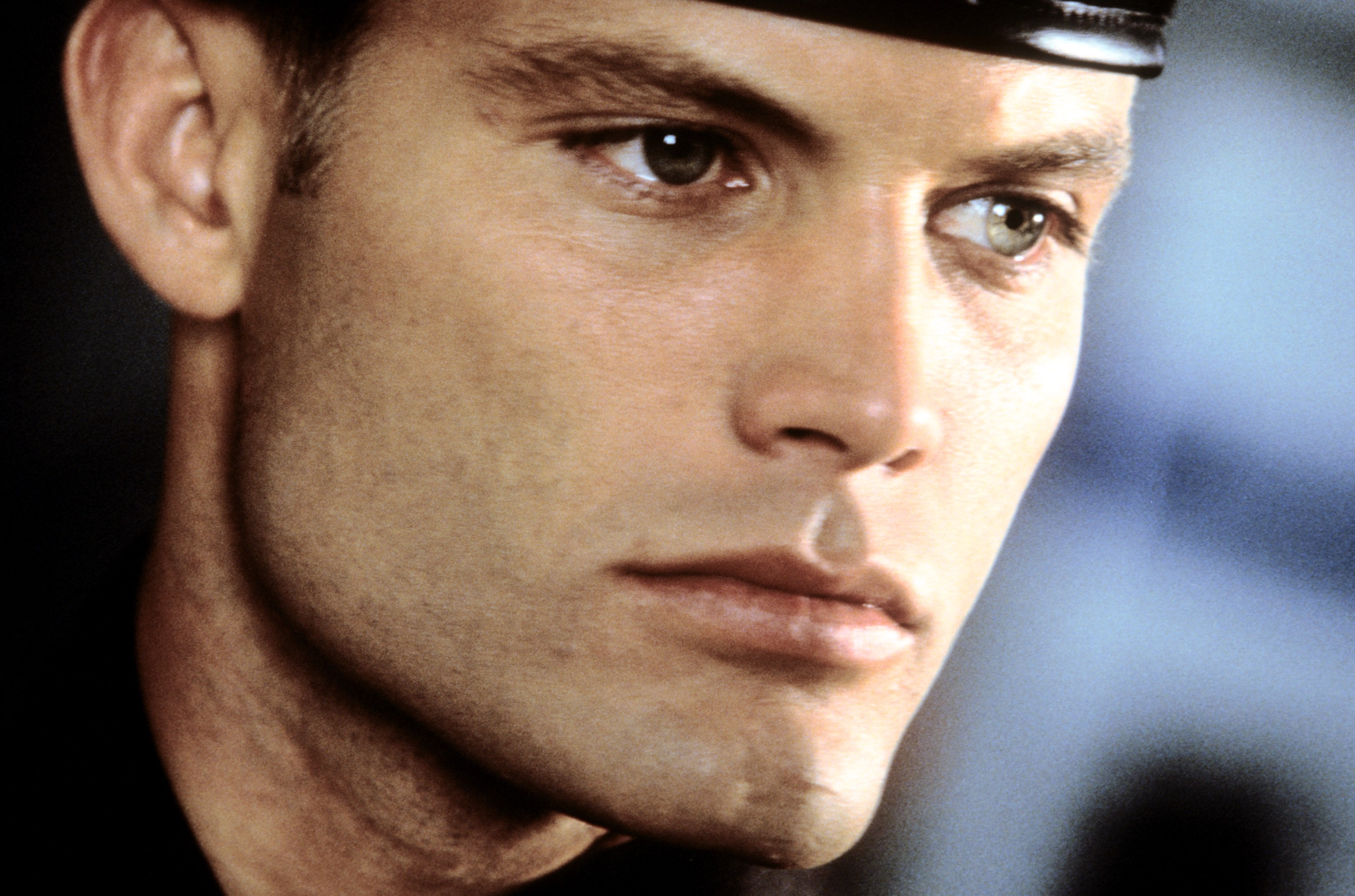 A person wearing a cap is shown in a close-up image, looking to the side with a serious expression