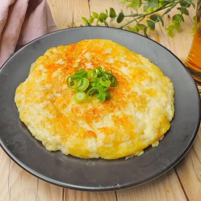 お皿に盛られたジャガイモとチーズのパンケーキ、ネギがトッピング。横に飲み物と緑の飾りがある。