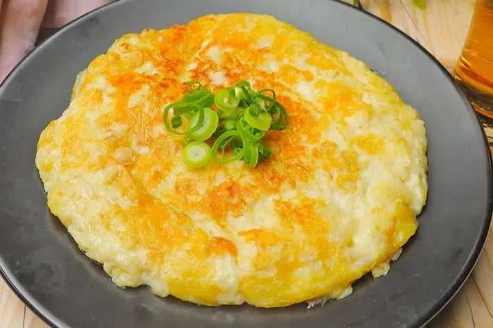 じゃがいもとチーズのガレット、ネギがトッピングされた黒い皿に盛られた料理。隣に飲み物。