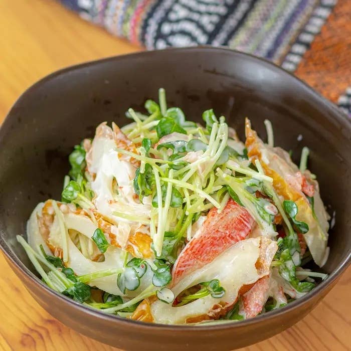 野菜とカニのサラダが黒いボウルに盛られている。上には新鮮なスプラウトがトッピングされている。