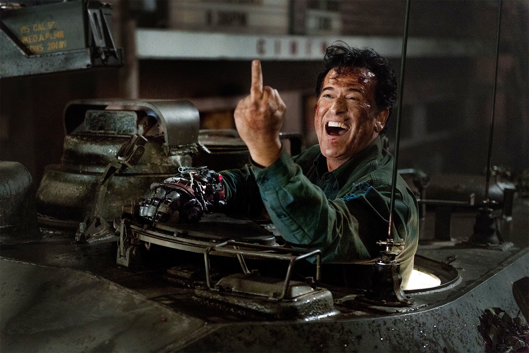 A person in a military tank smiles while making a hand gesture with a mechanical glove. It appears to be from an action movie scene