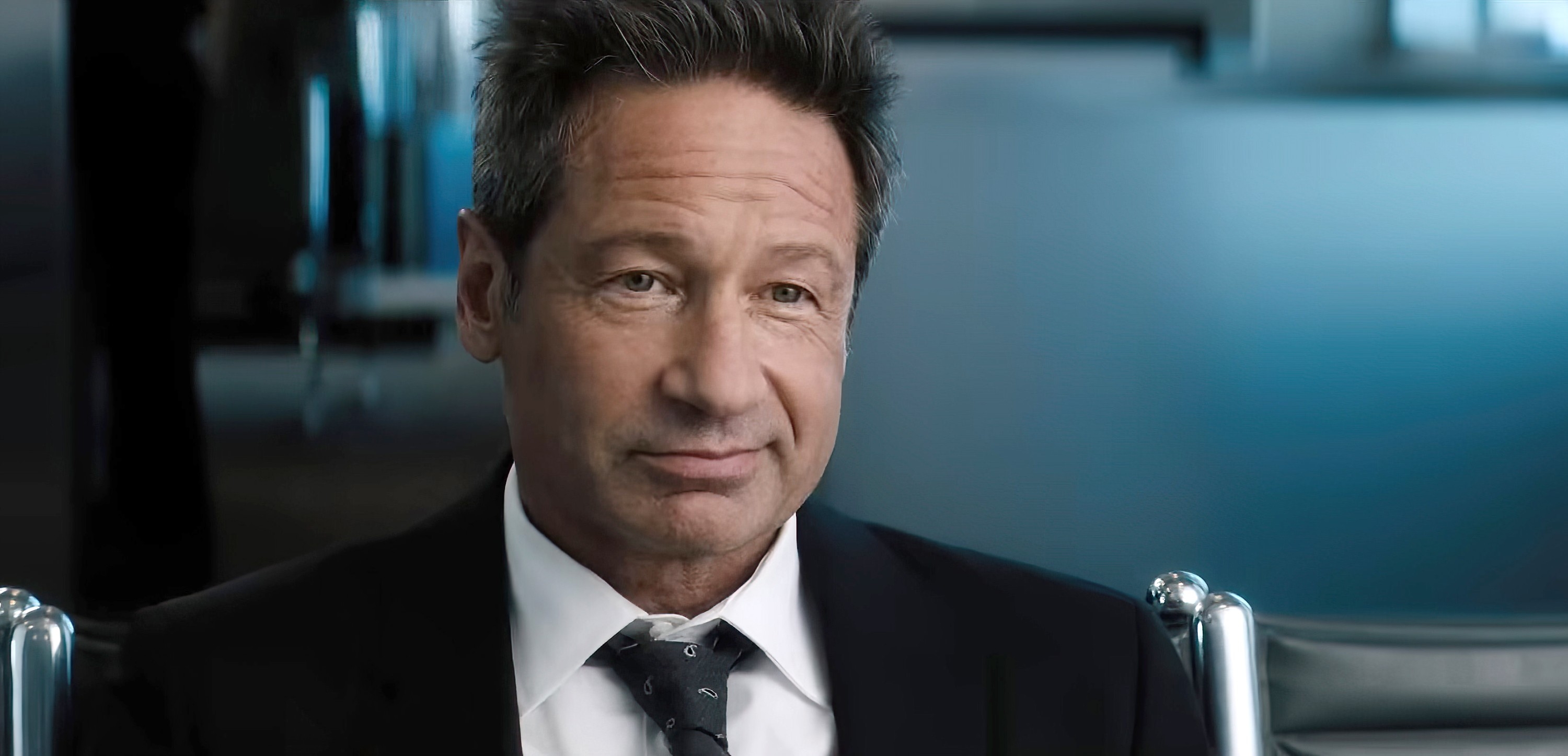 Person in a suit seated, looking contemplative, with a blurred background