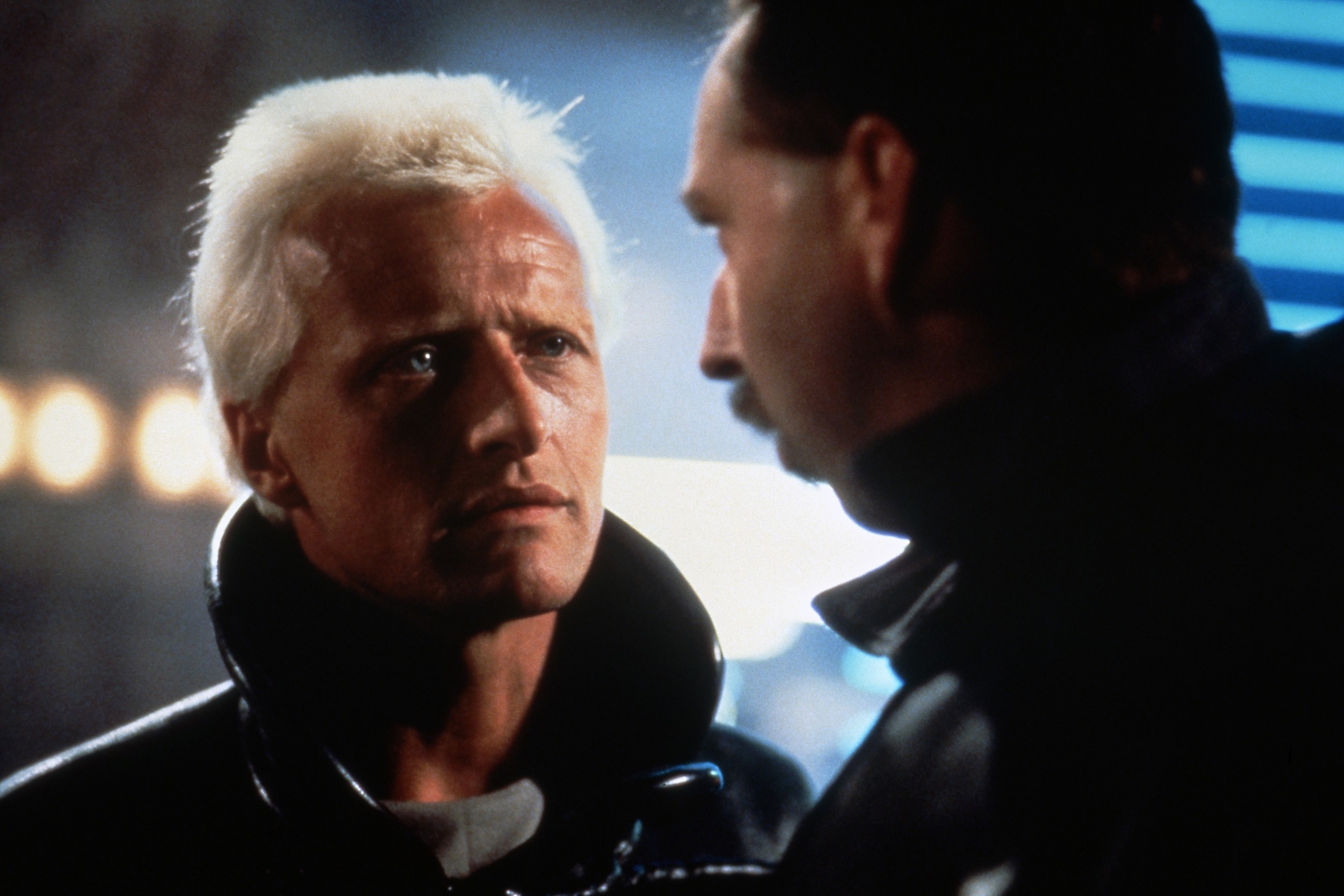 Two people in a tense conversation, one with short, light hair and an intense expression, the other with a mustache and side view