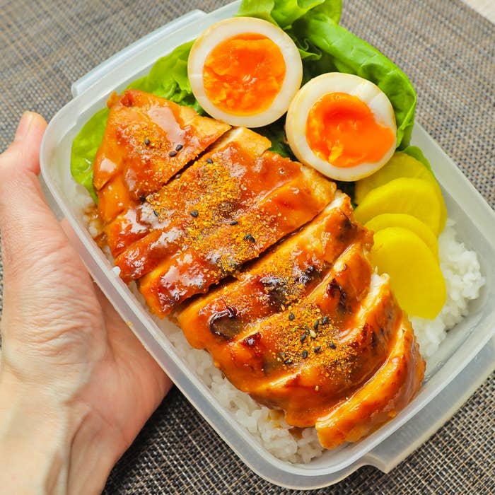 弁当箱に盛られた焼き鳥、ご飯、煮卵、漬物、レタスが入ったおいしそうな食事。