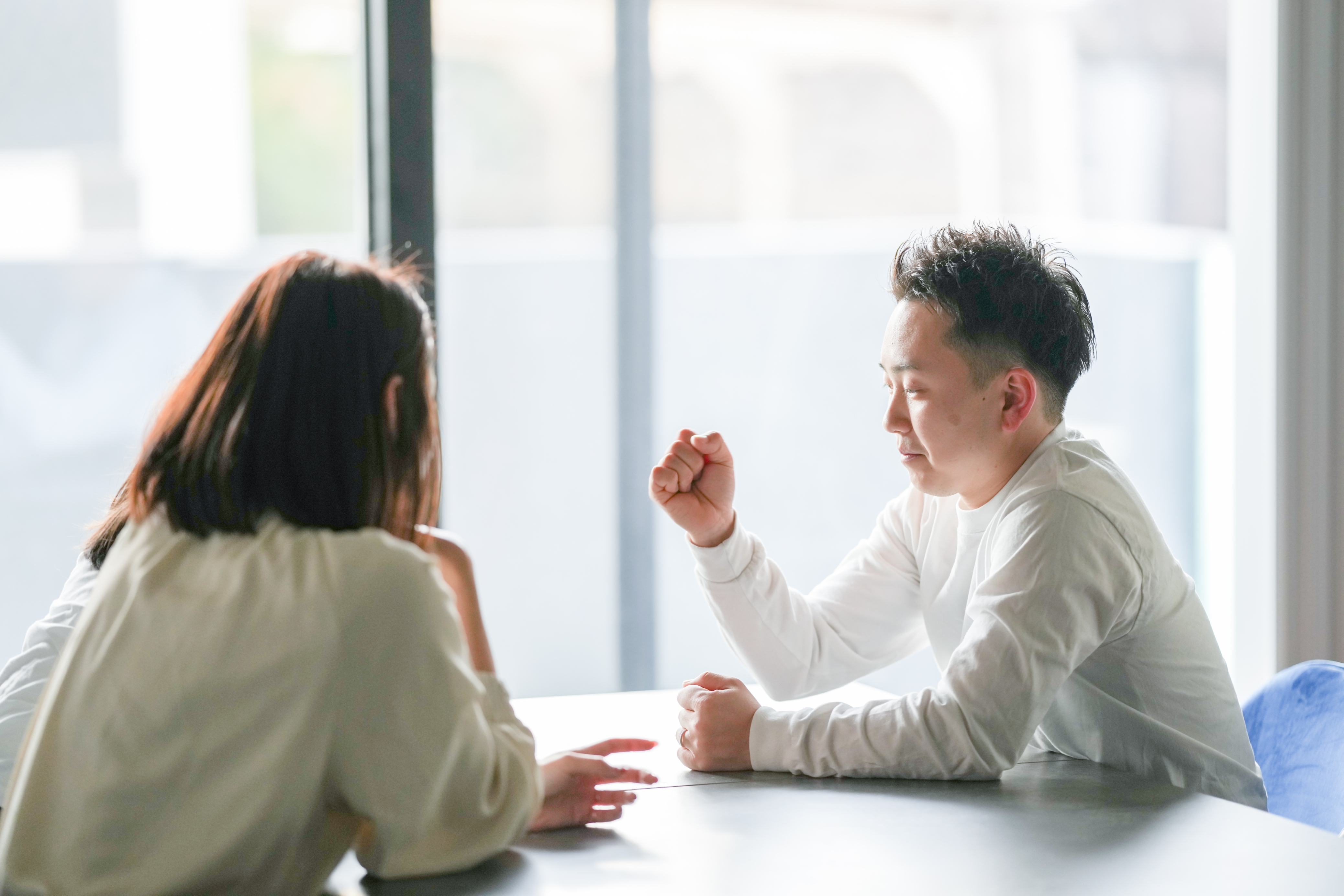 テーブルに向かい合って座り、会話している2人の人物。ビジネスミーティングか相談中の様子。