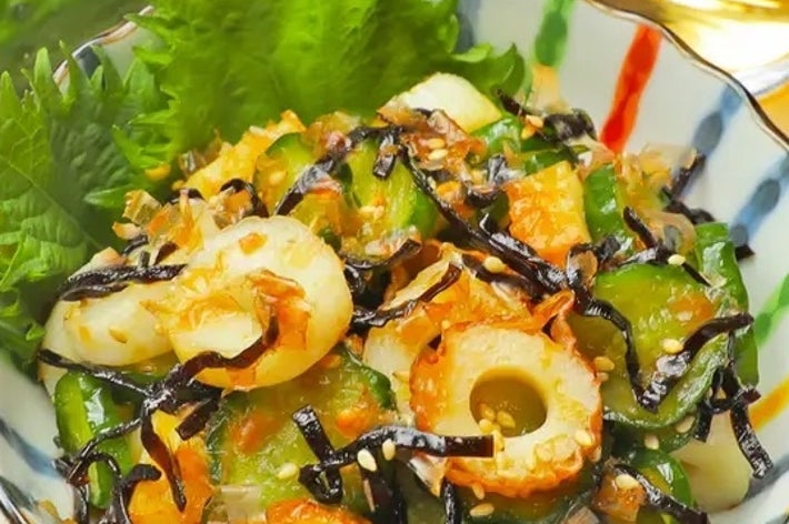 きゅうり、ちくわ、昆布の和風サラダが器に盛られています。背景にはきゅうりと飲み物が置かれています。