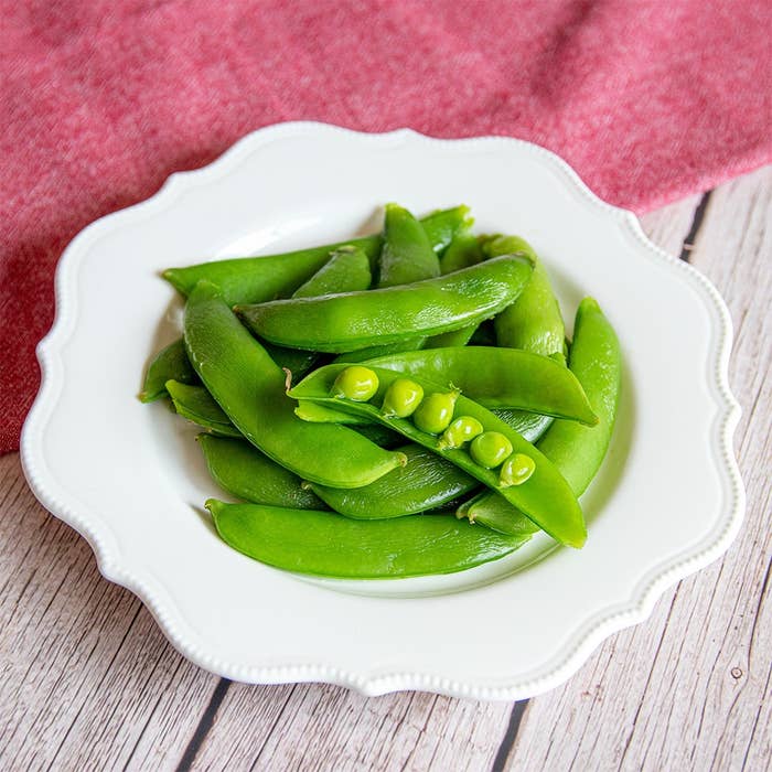 白い皿に盛られたスナップエンドウが木目のテーブルに置かれている。