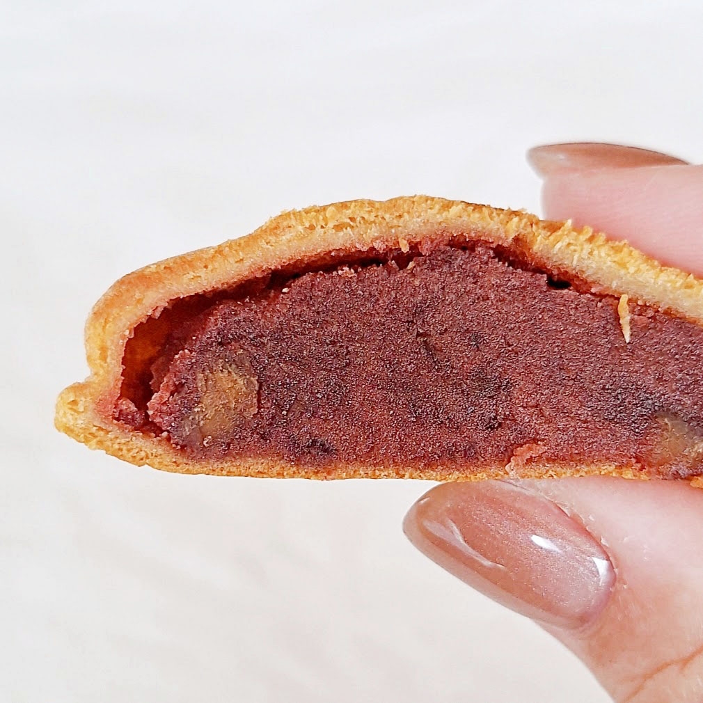 手で持った断面が見える焼き菓子。中に餡のようなものが詰まっている。