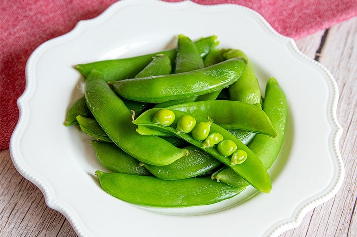 皿に盛られた新鮮なスナップエンドウがテーブルに置かれている。