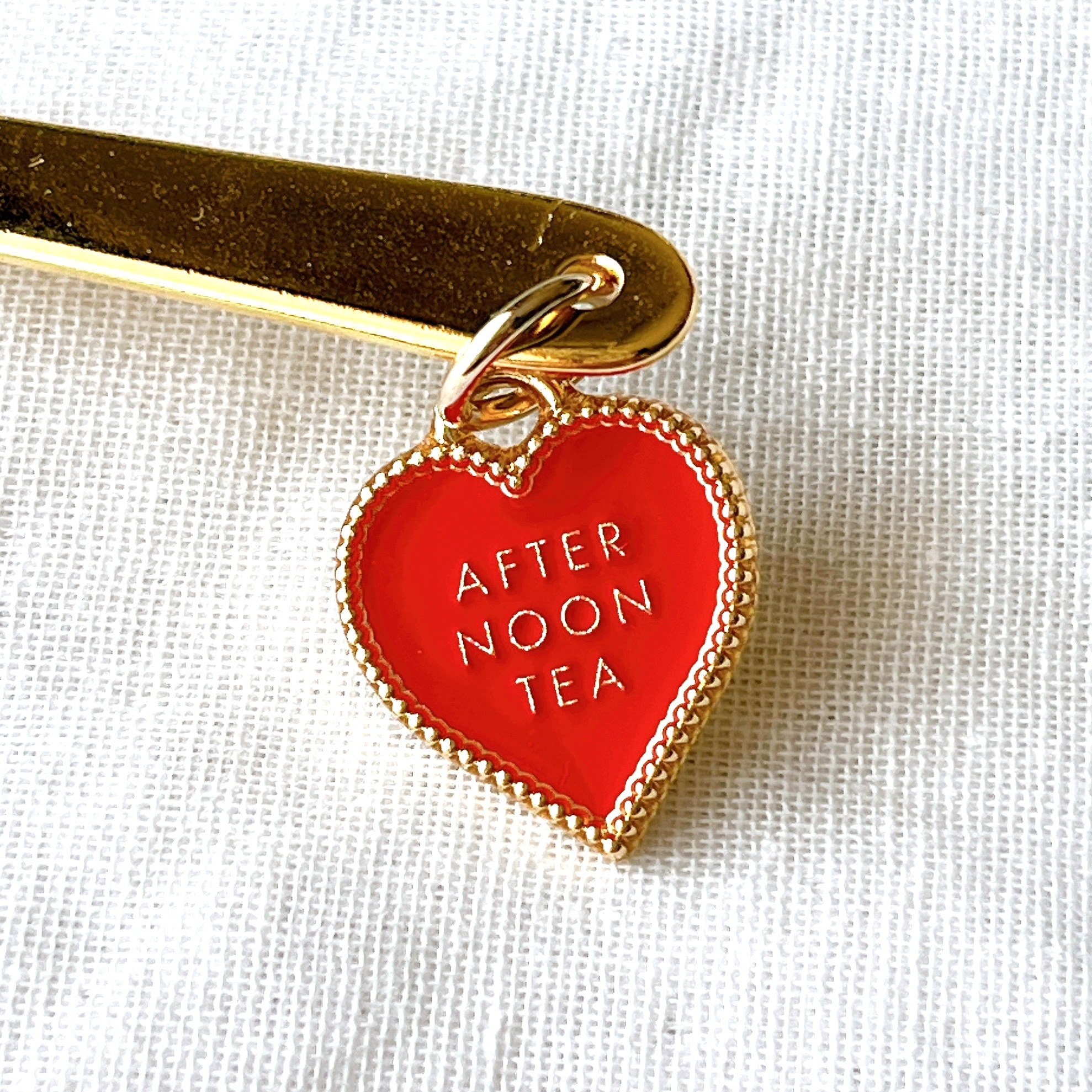 ハート型のチャームに「AFTERNOON TEA」と刻まれている。金色のフックに付いている。