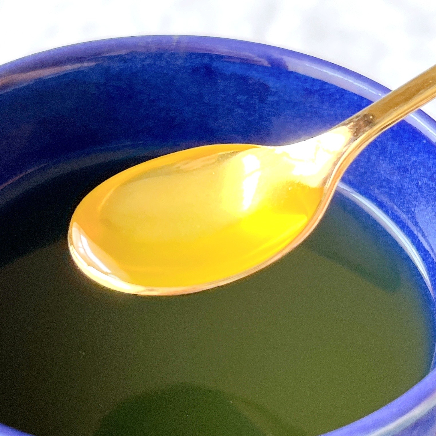 カップに濃い飲料が入っており、金色のスプーンが液体の上に浮かんでいます。