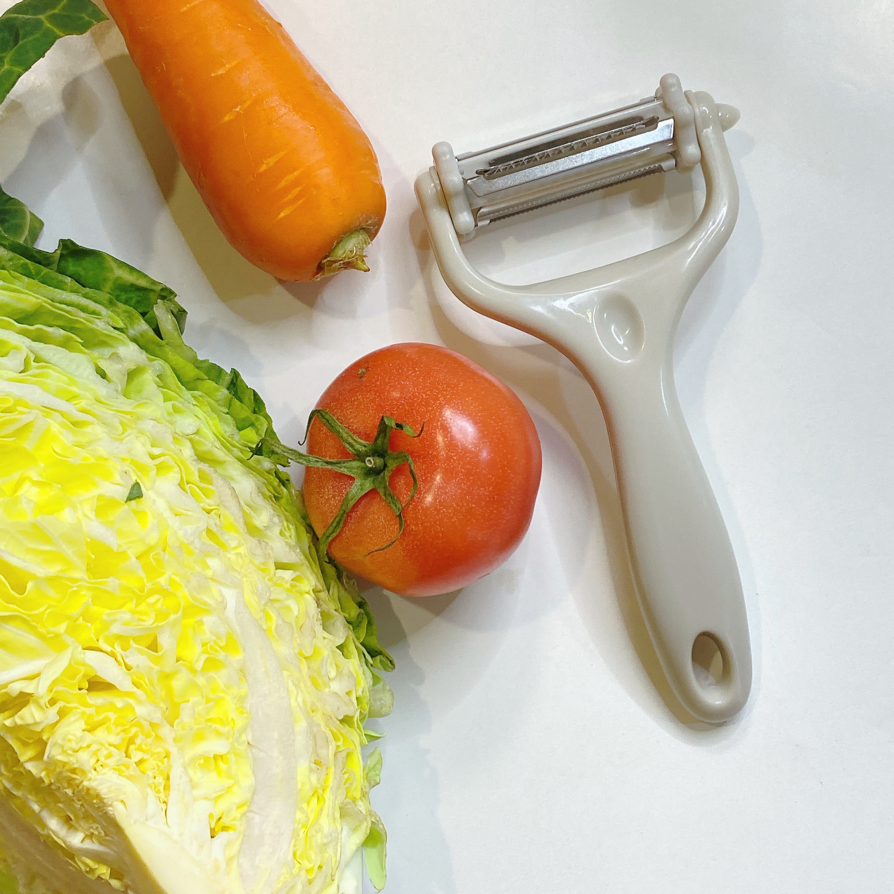 キャベツ、トマト、にんじんとピーラーが並べられたキッチンカウンター。