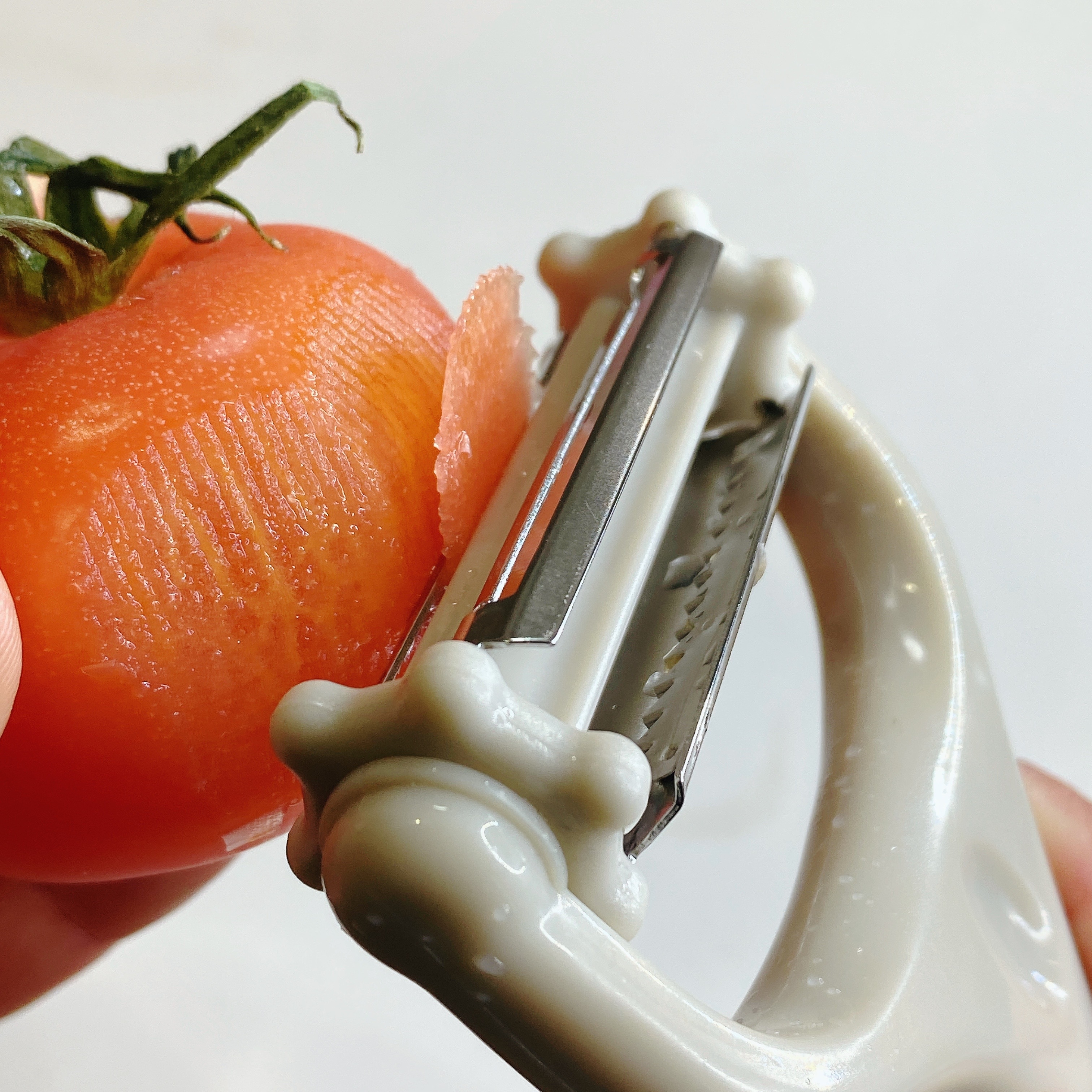 トマトの皮をピーラーでむいている様子。